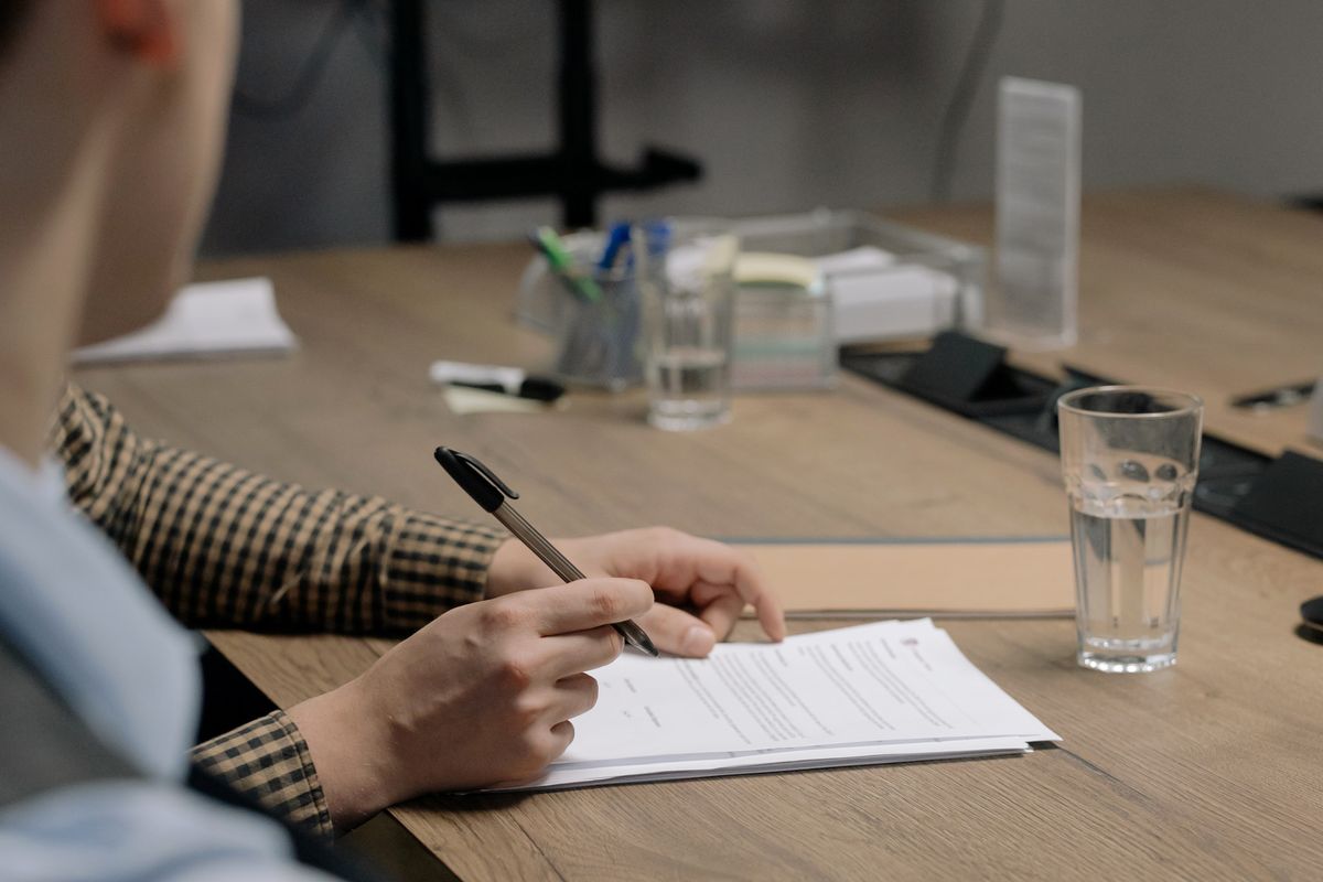 A person in business attire signing a document at a wooden desk