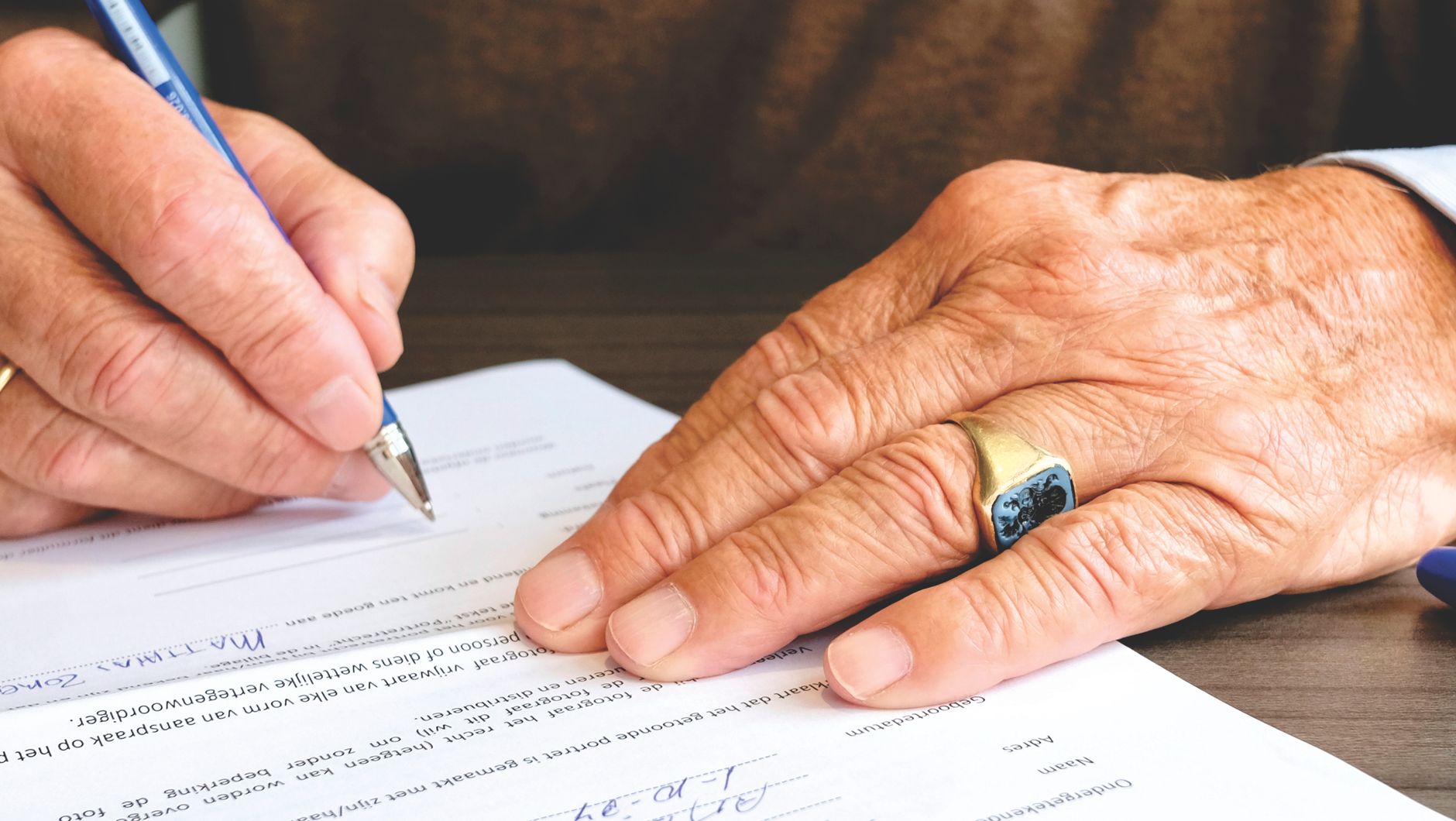 An elderly person’s hands signing a document with a pen